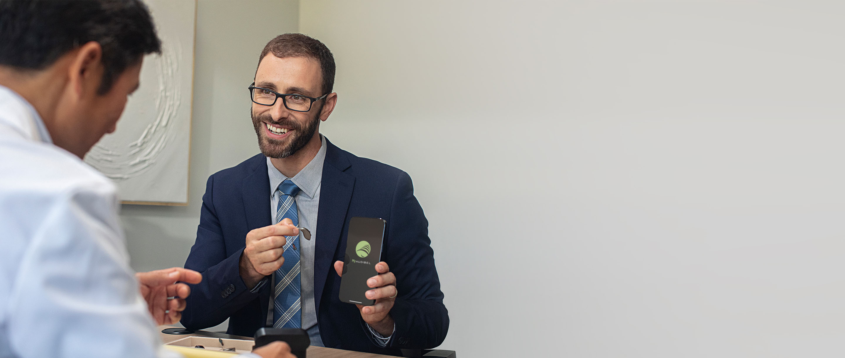 A man holding a hearing aid and a mobile phone with the My Audibel app on it's screen