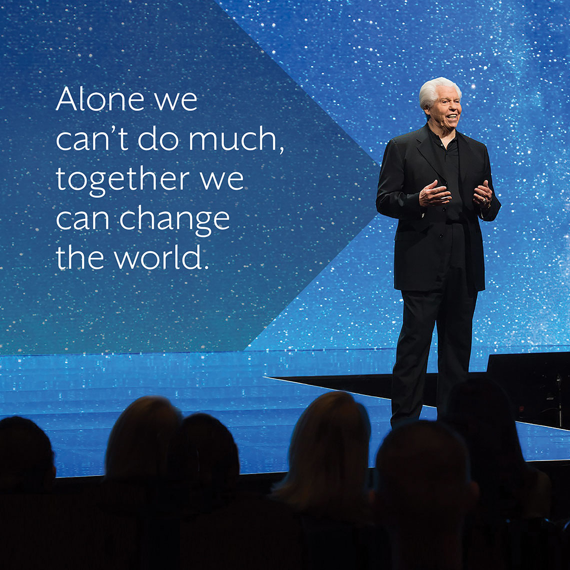Bill Austin standing on a stage next to the quote 'Alone we can't do much, together we can change the world.'